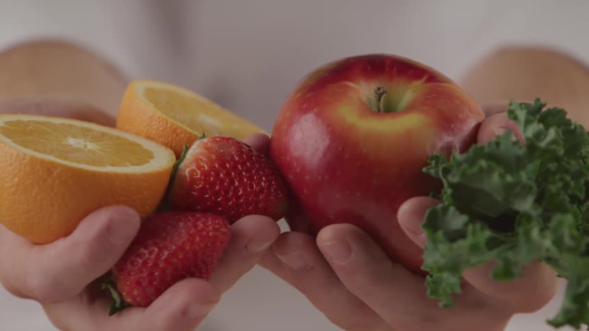 A person holds several pieces of fruit in their hands as well as a leaf of lettuce