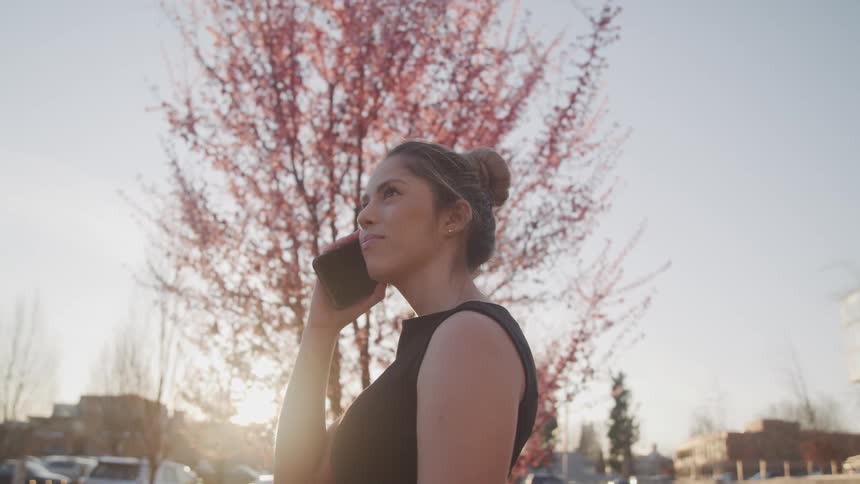 A woman is talking on her cell phone by a tree