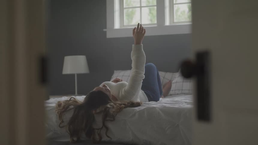 A female laying on a bed moving her arm in the air