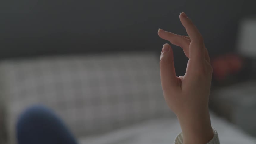 A female lying in bed with her hand in the air moves her fingers slowly