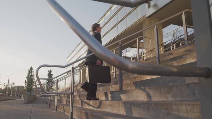 Businessman with a suit and carrying a briefcase climbs up stairs to the office building