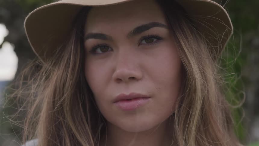 Woman with brown hair and a brown hat faces the camera with eye contact