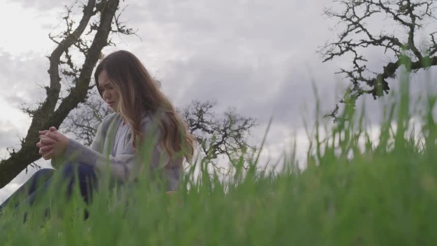 Young woman sits in the grass outdoors holding her hands in prayer