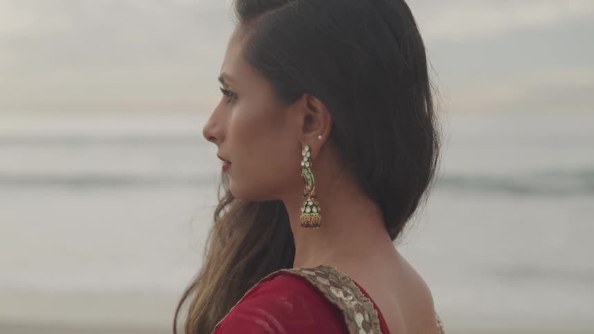 A young indian woman in traditional clothing looks out at the ocean while standing on the beach during the day