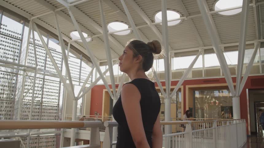 A woman in a shopping mall stands against a railing and looks outside