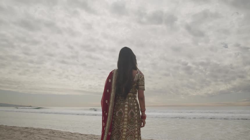 A woman standing on the beach looks out at the water