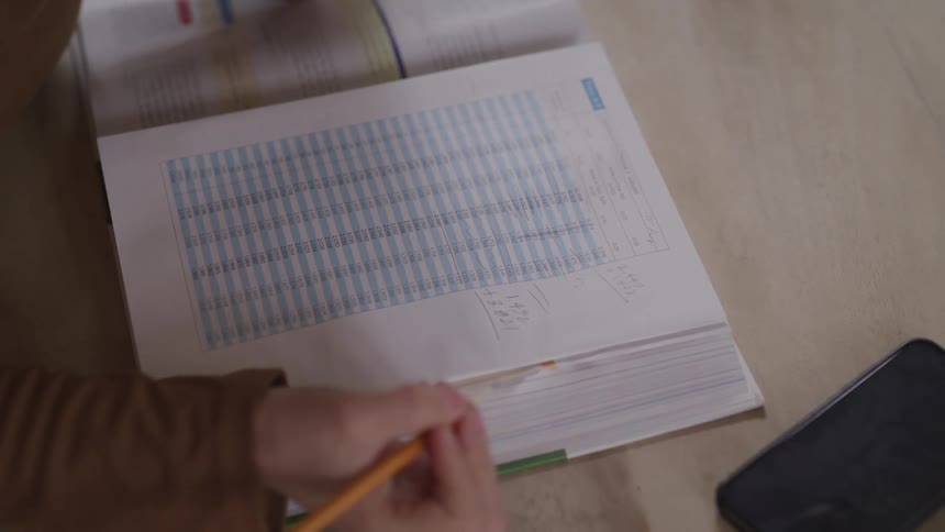 A person sitting a table with a textbook reviews a printout