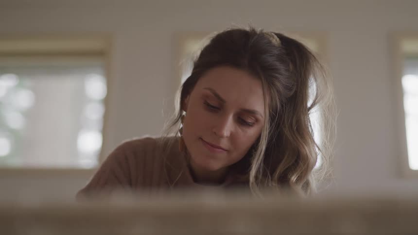 Woman with brown hair and a sweater sits on bed and reads a book
