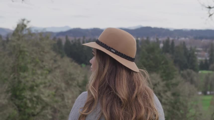 Woman with brown wavy hair and a hat watches the horizon on a cloudy day