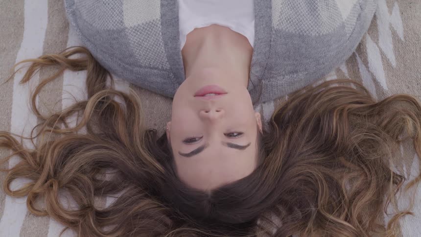 Woman with brown hair lies down on a rug opens her eyes