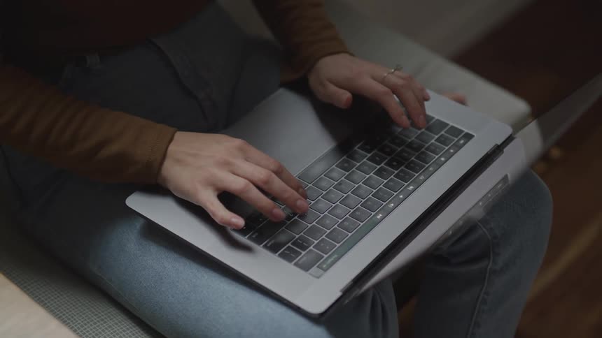A woman types on a laptop sitting on her laptop