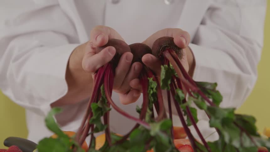 A chef holding beets over a table with produce