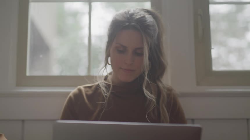A woman is using her laptop by the window