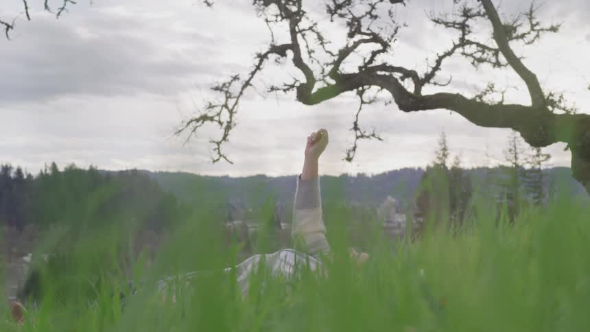 A teenage girl lying in the grass reaches her arm up towards the sky