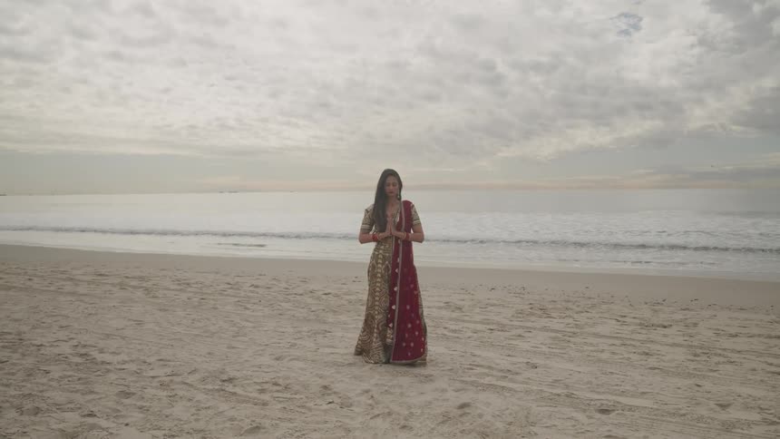 A female standing on a beach meditating with folded hands