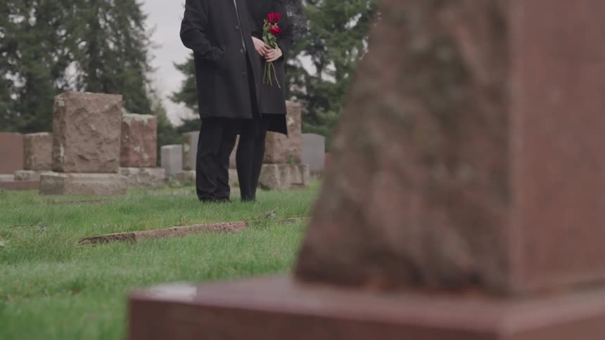 Two people wearing black standing in a cemetery with trees and the sky in the background