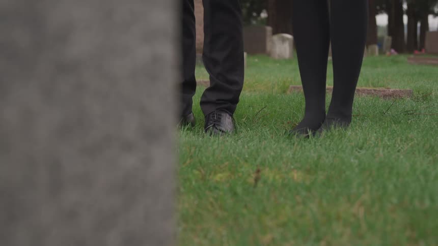 A man and woman standing in front of a headstone at a cemetery