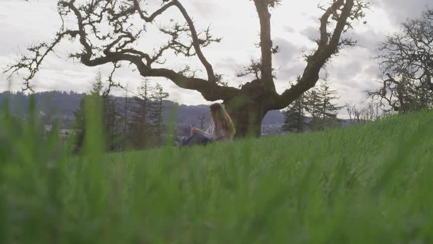 A young woman sits outdoors underneath a leafless tree