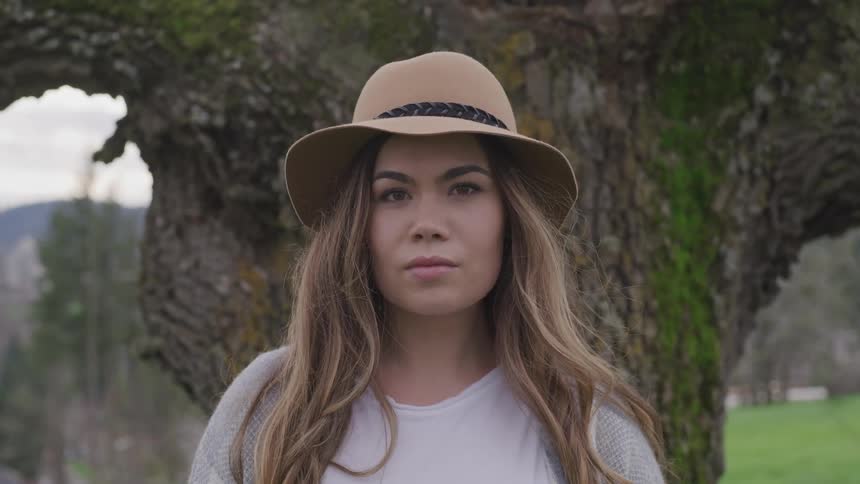 A teenage girl standing in front of a large tree looks up
