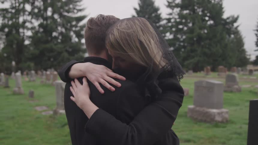 Man and woman hug as they stand in a cemetery