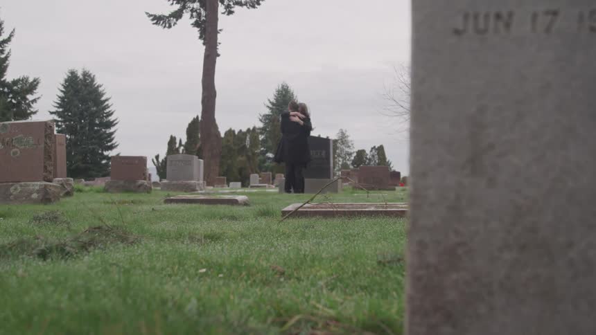A couple at a cemetery grieving near a grave