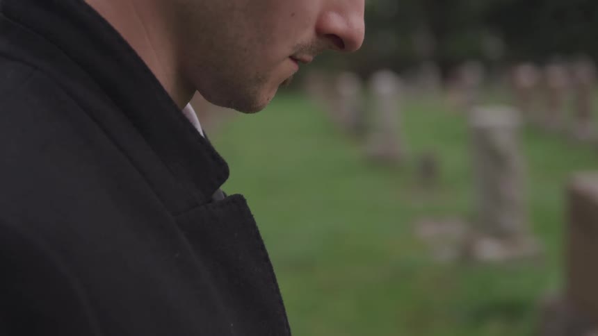 A man standing in a cemetery with his head bowed down