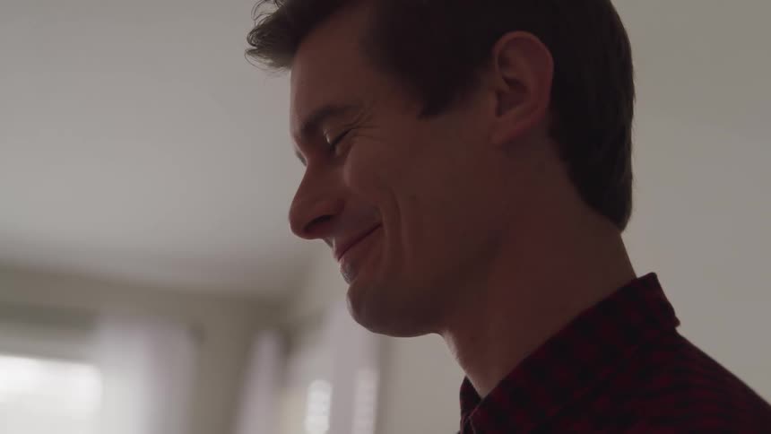 A man standing and smiling in a room with windows in the background