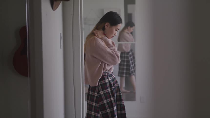 A young woman walks barefoot across a room while looking downward lost in thought