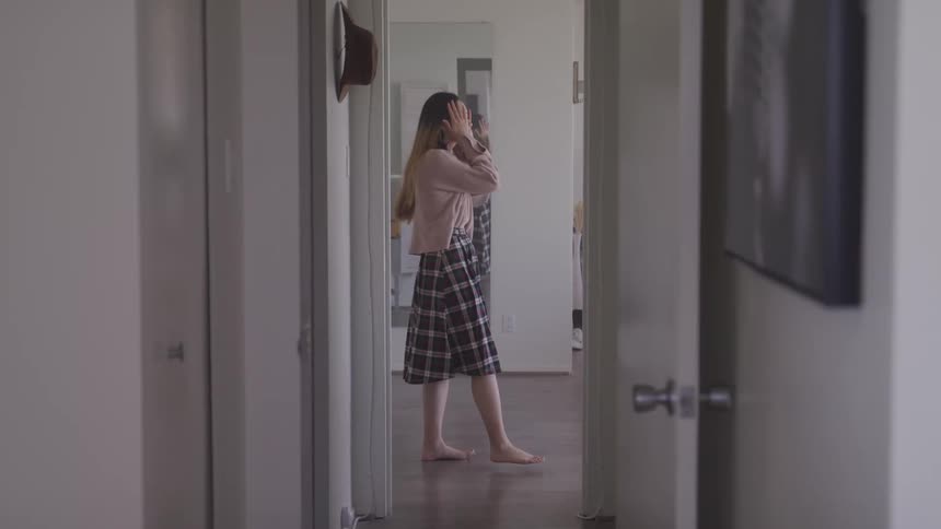 A woman walks in front of a mirror with her hands on her head