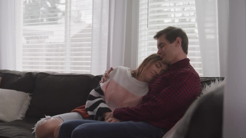 A man embraces a woman as they rest together on a sofa during the day