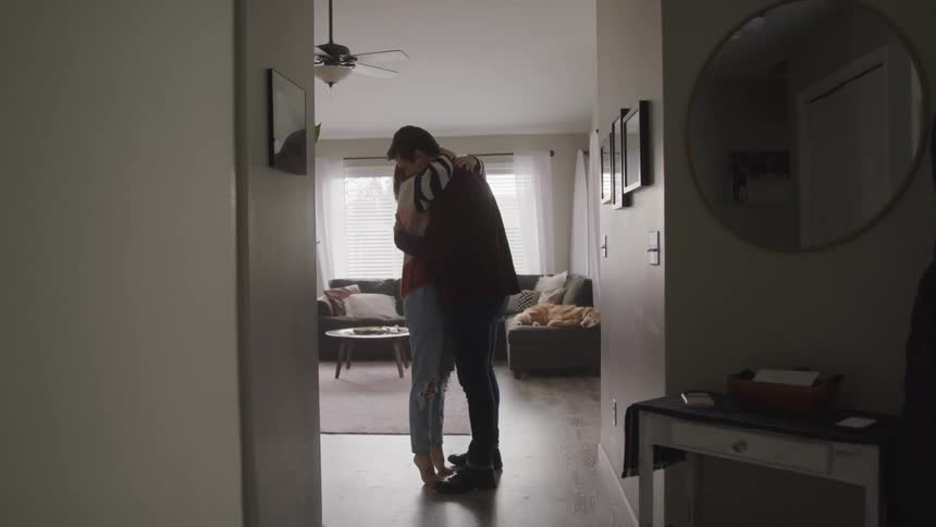 A man and woman tenderly embrace each other in a living room