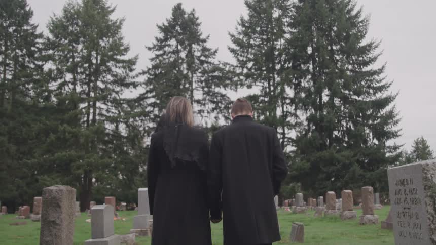 Man and woman hold hands as they walk through a cemetery
