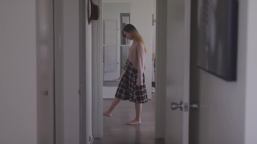 A woman with a skirt walking by a doorway with a mirror in the background