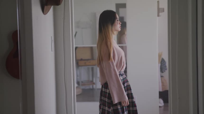 A woman with a skirt walking by a doorway with a mirror in the background