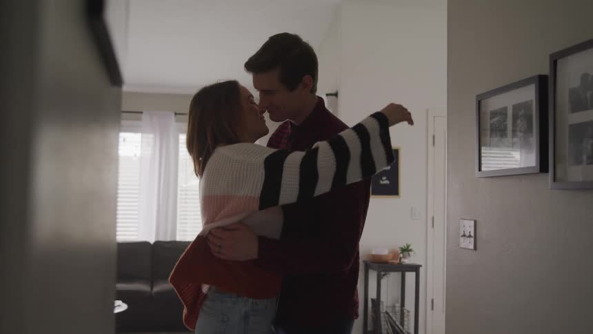 Man with a shirt and woman with a sweater look into each others eyes and cuddle one another in living room at home