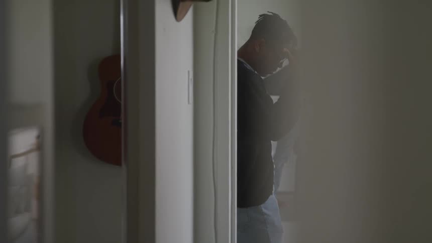 Black man with glasses holds his forehead and walks in the house