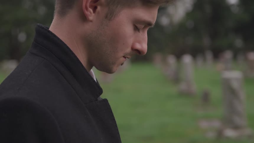 Man stands in cemetery praying with head bowed and eyes closed