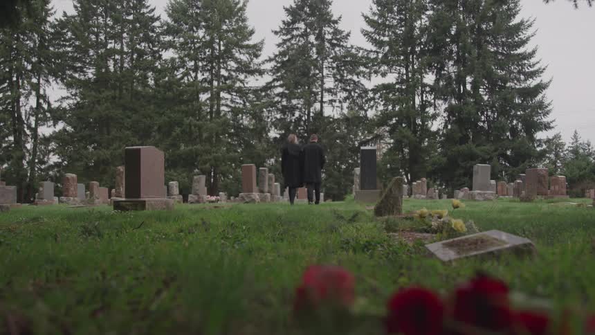 A man and woman stand at a grave site solemnly