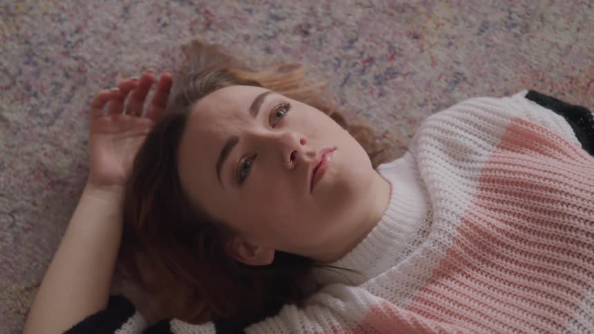Woman with brown hair and a sweater lies down on a carpet and looks up at the ceiling