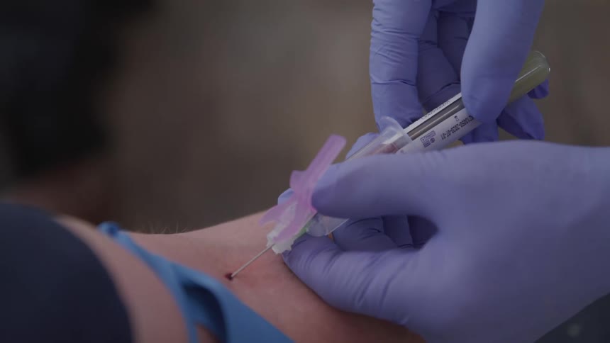 A medical person takes a vile of blood from a needle in a patient
