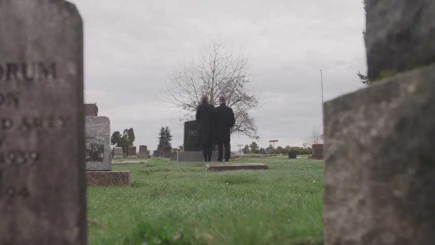 A couple in a cemetery standing at a tombstone