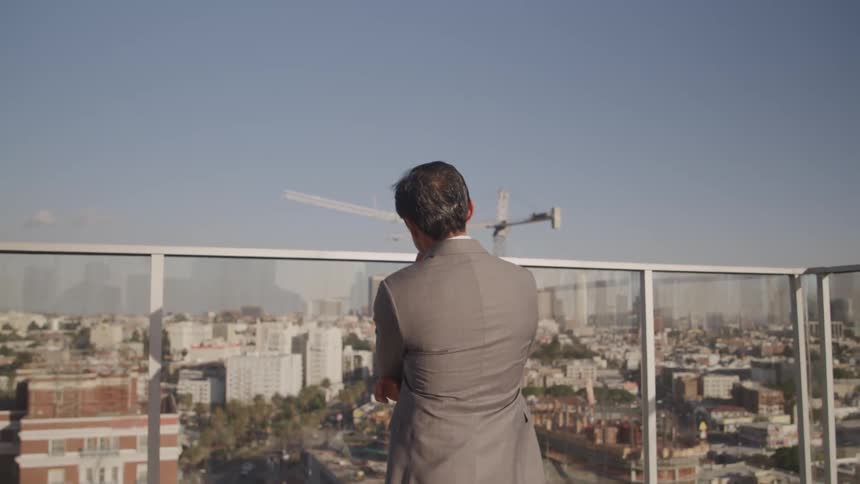 Asian businessman stands and watches city skyline on office balcony