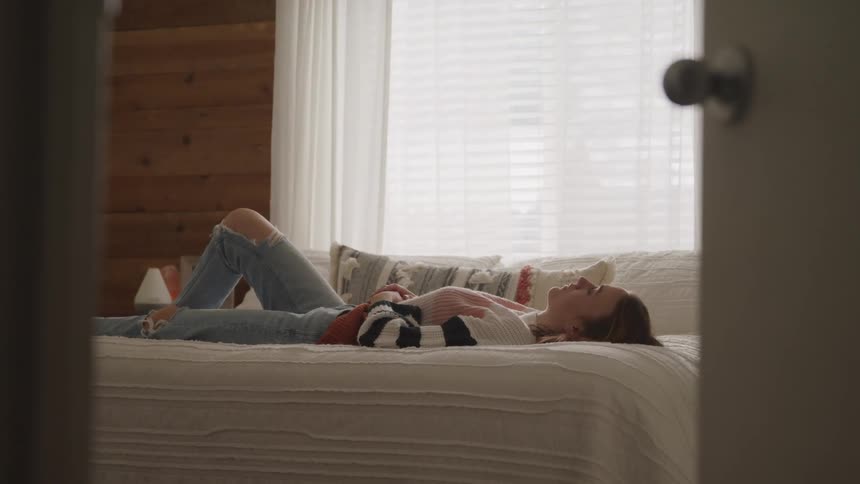 Woman with brown hair a sweater and jeans lies down on the bed