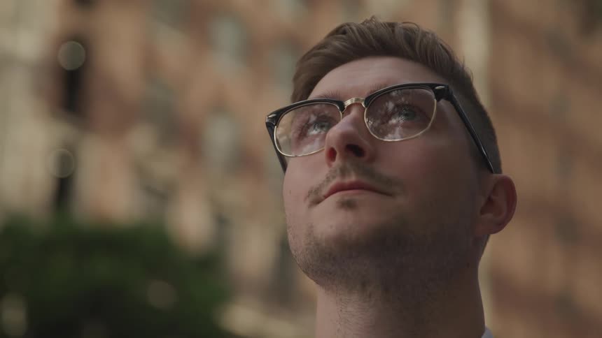 A young man gazes up at his surroundings while standing outdoors in a metropolis