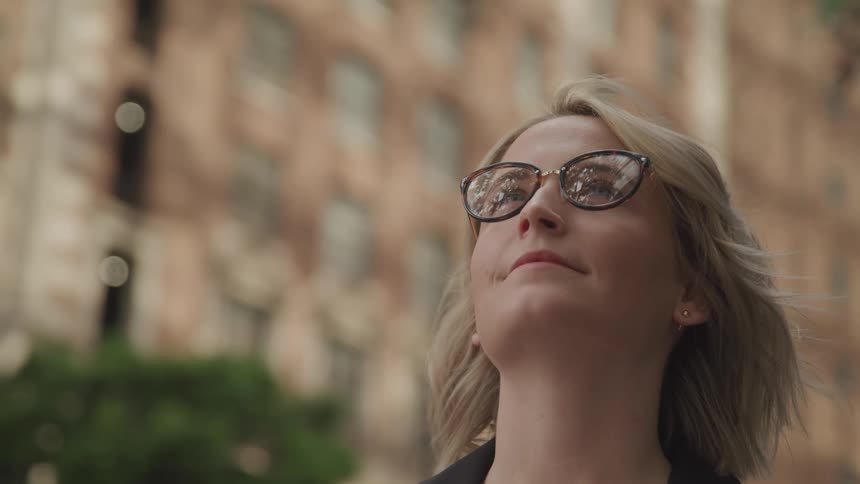 A woman standing in a downtown area looks up at the high rise buildings