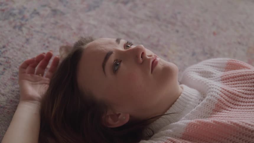 Woman with brown hair and a sweater lies down on the carpet and looks at the ceiling