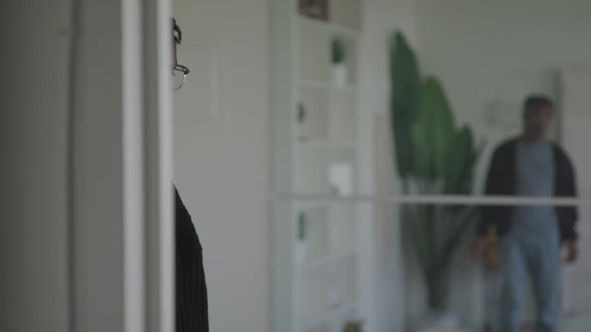 A man walks down a hallway in his apartment and turns back around and smiles
