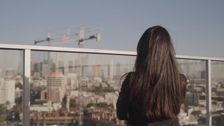 A woman is standing on a balcony in a downtown city