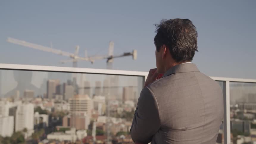 A man stands on a rooftop and looks at the city skyline with high rise buildings and a construction crane