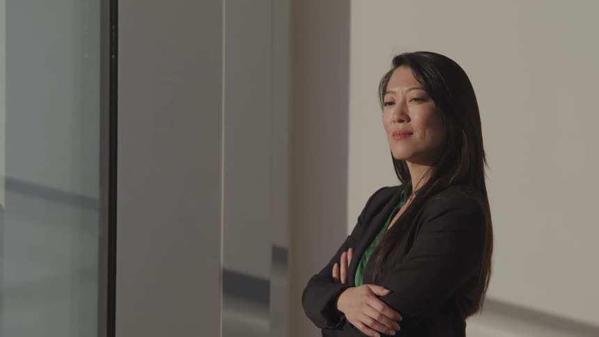 Asian businesswoman with a black blazer and arms crossed looks into space in the office